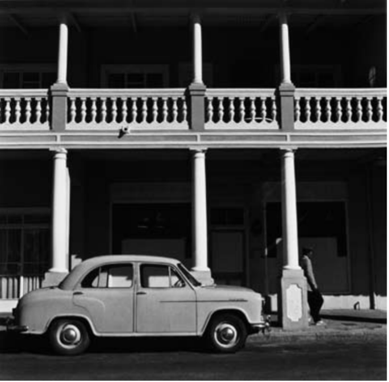 Black and white photo of car in front of double story building