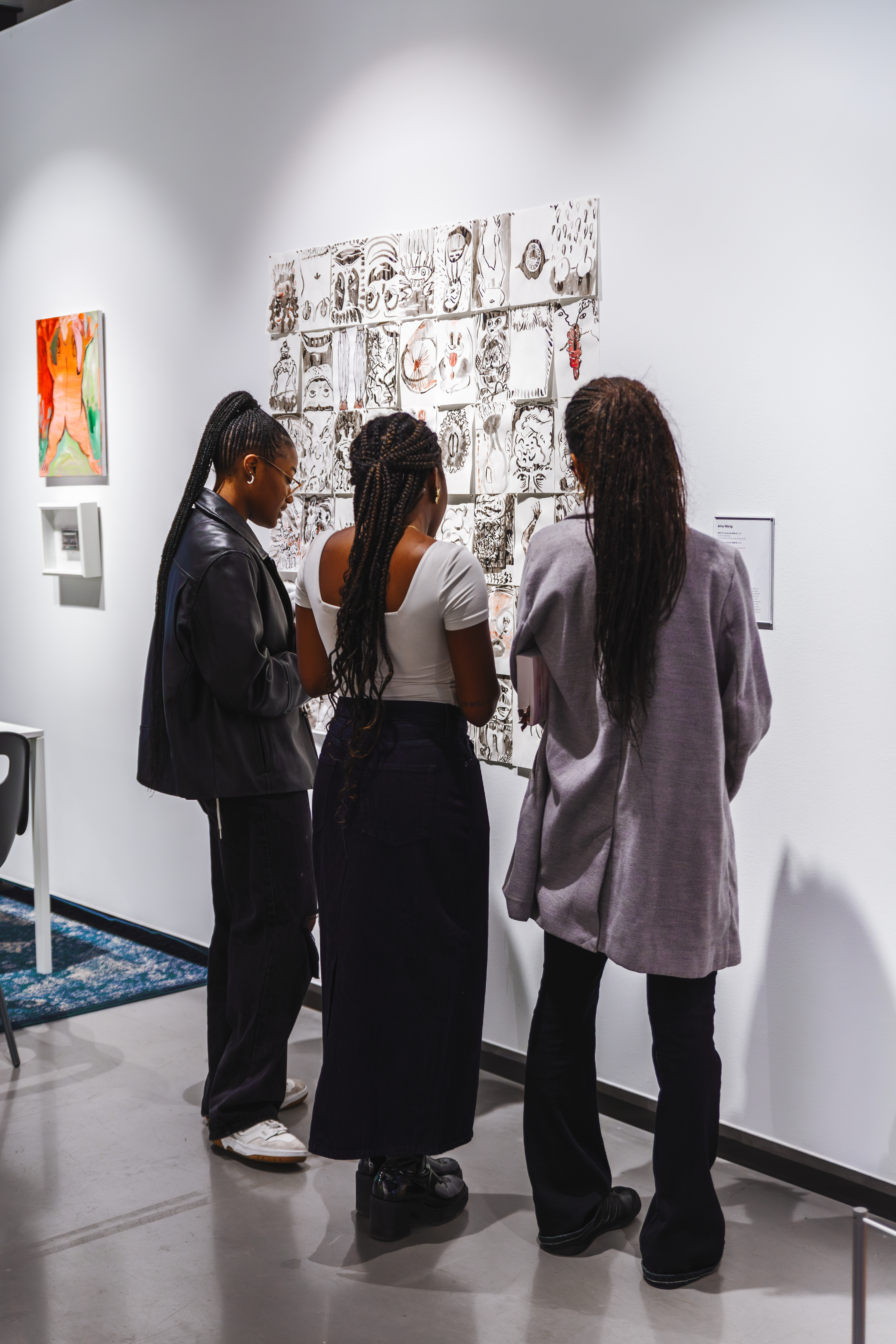 An image of three women looking at series of paper painting on a wall