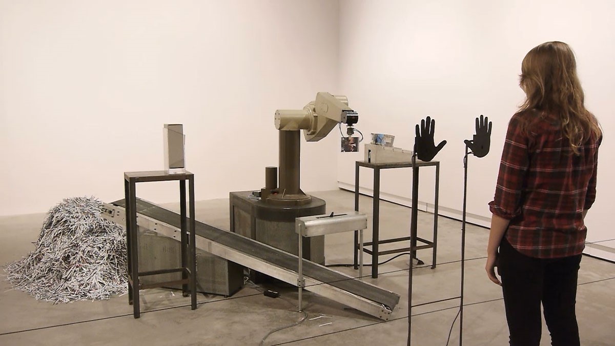 A photograph of a person facing a machine in a gallery room.