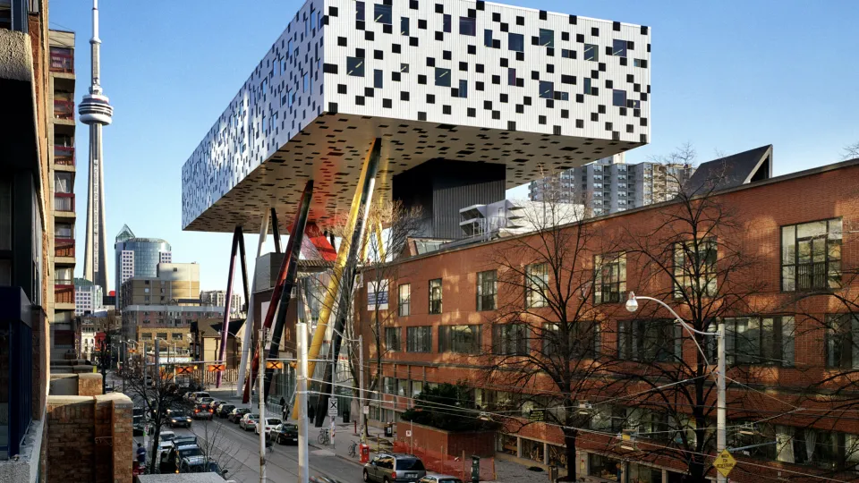 Street view of black and white checkered building on stilts beside a brick lowrise.