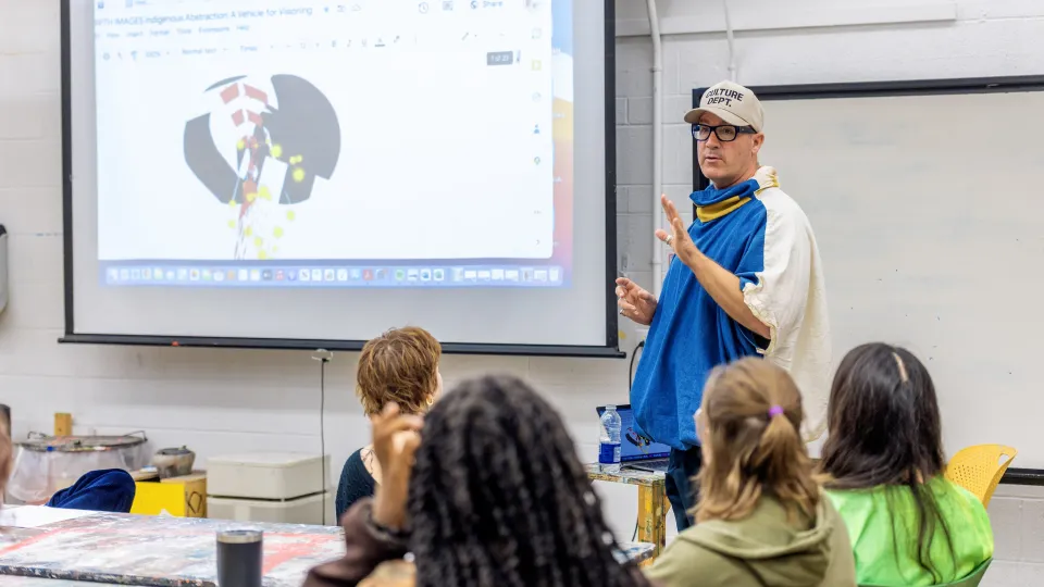 A professor standing next to a projection screen in front of a group of students.