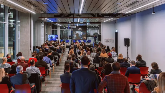 Large room with people sitting in rows of red chairs.