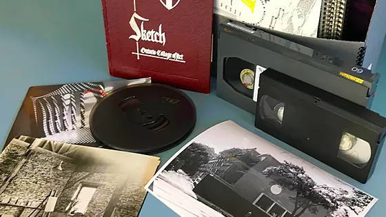 A book, a record, a VHS tage, and some papers on a blue table.