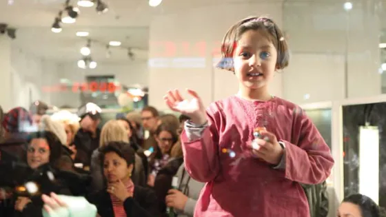 A girl with headphones stands in a room of people