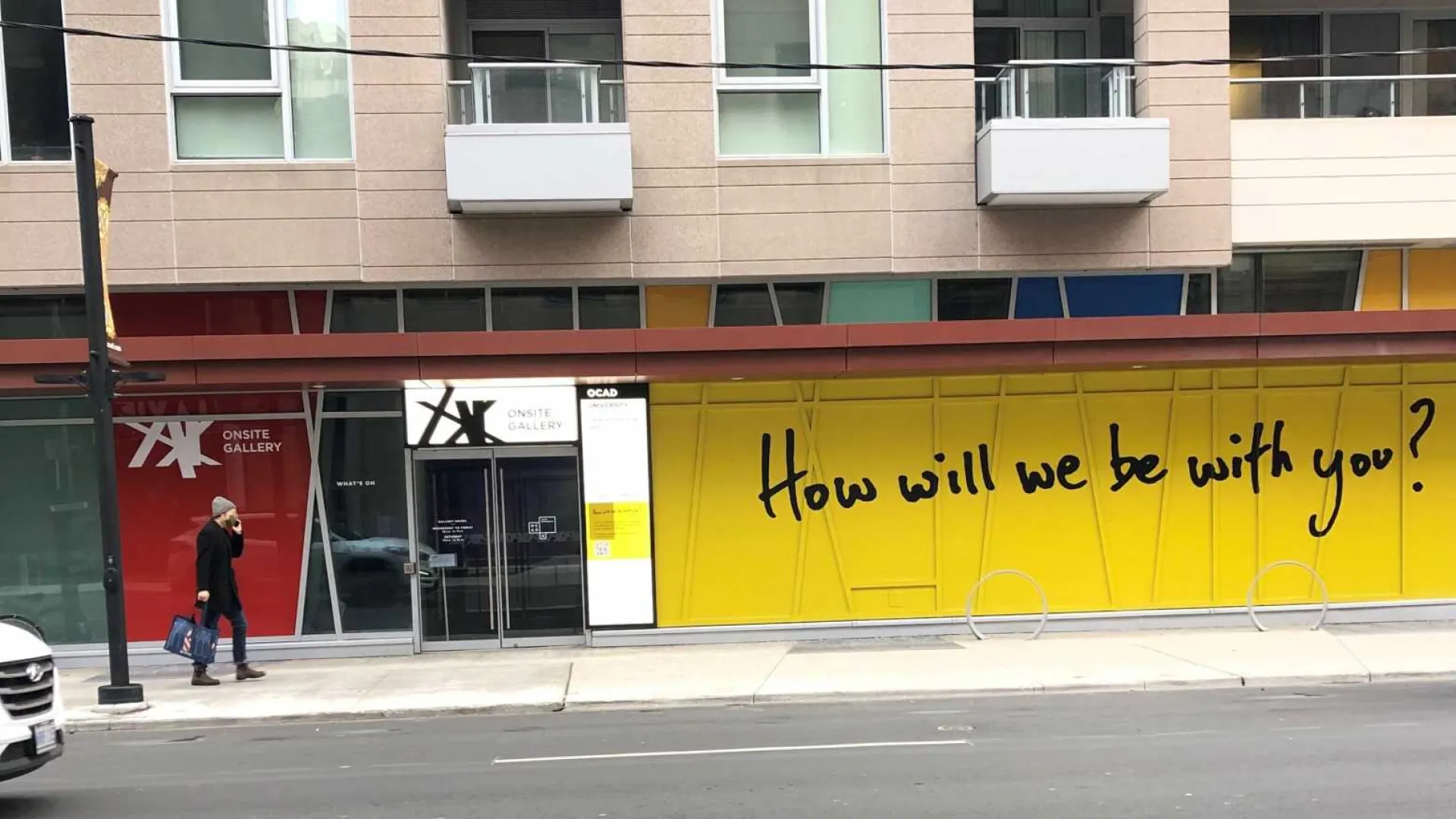 How will we be with you written in black on yellow background painted on window of the onsite gallery