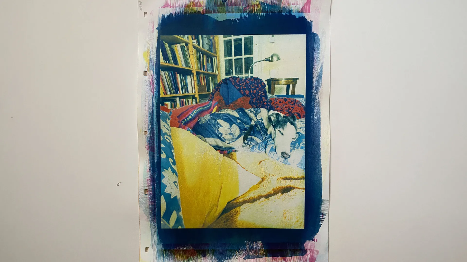 this is a colour print with a portrait orientation \ a black &amp; white dog \ S \ a whippet is centred \ laying on a couch snuggled in blankets &amp; pillows \ in the background there is a bookcase \ a light \ and a cup of tea to the right of the print is a handwritten poem \ which could be understood as the beginnings of an escape into drawing