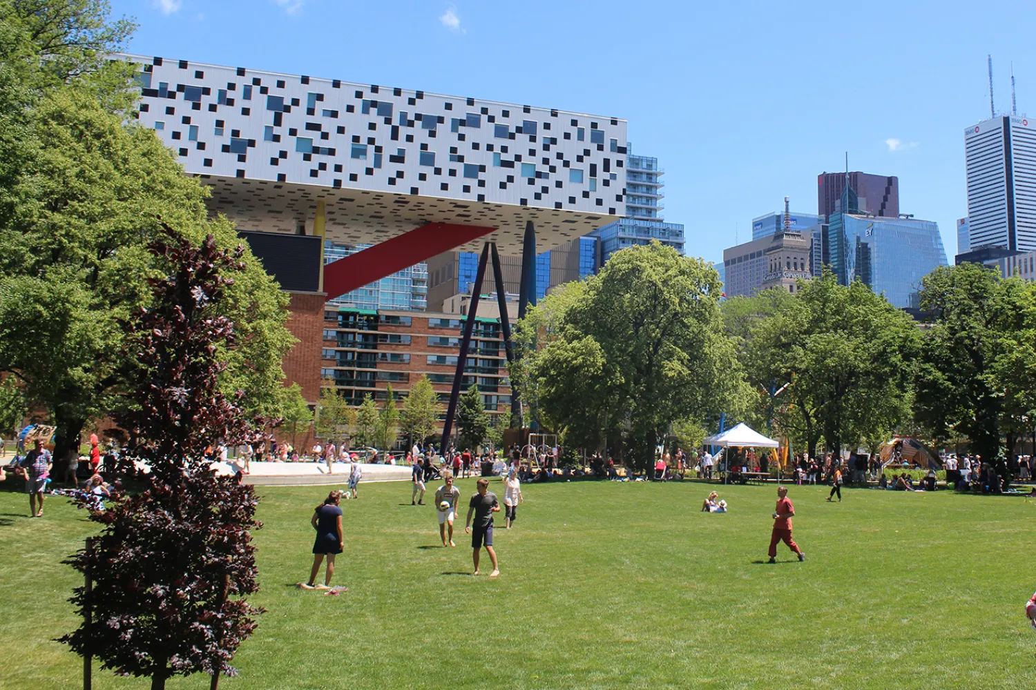 People on a field with a ball, in front of a white and black checkered building on stilts.