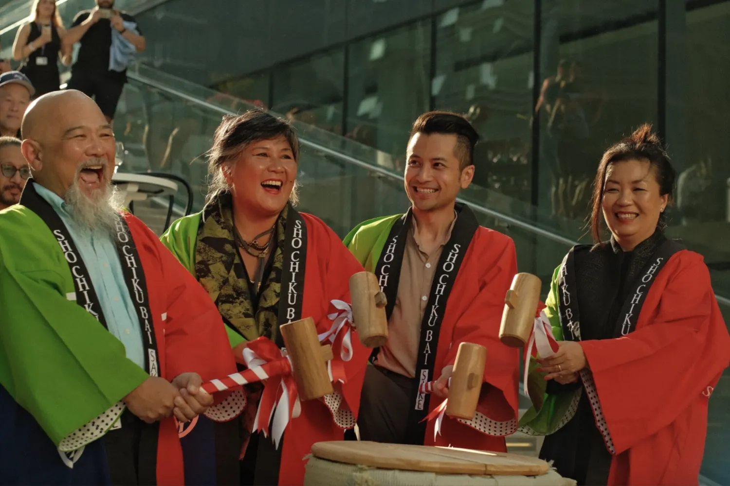 Four people in cultural adornment holding mallets over a drum.