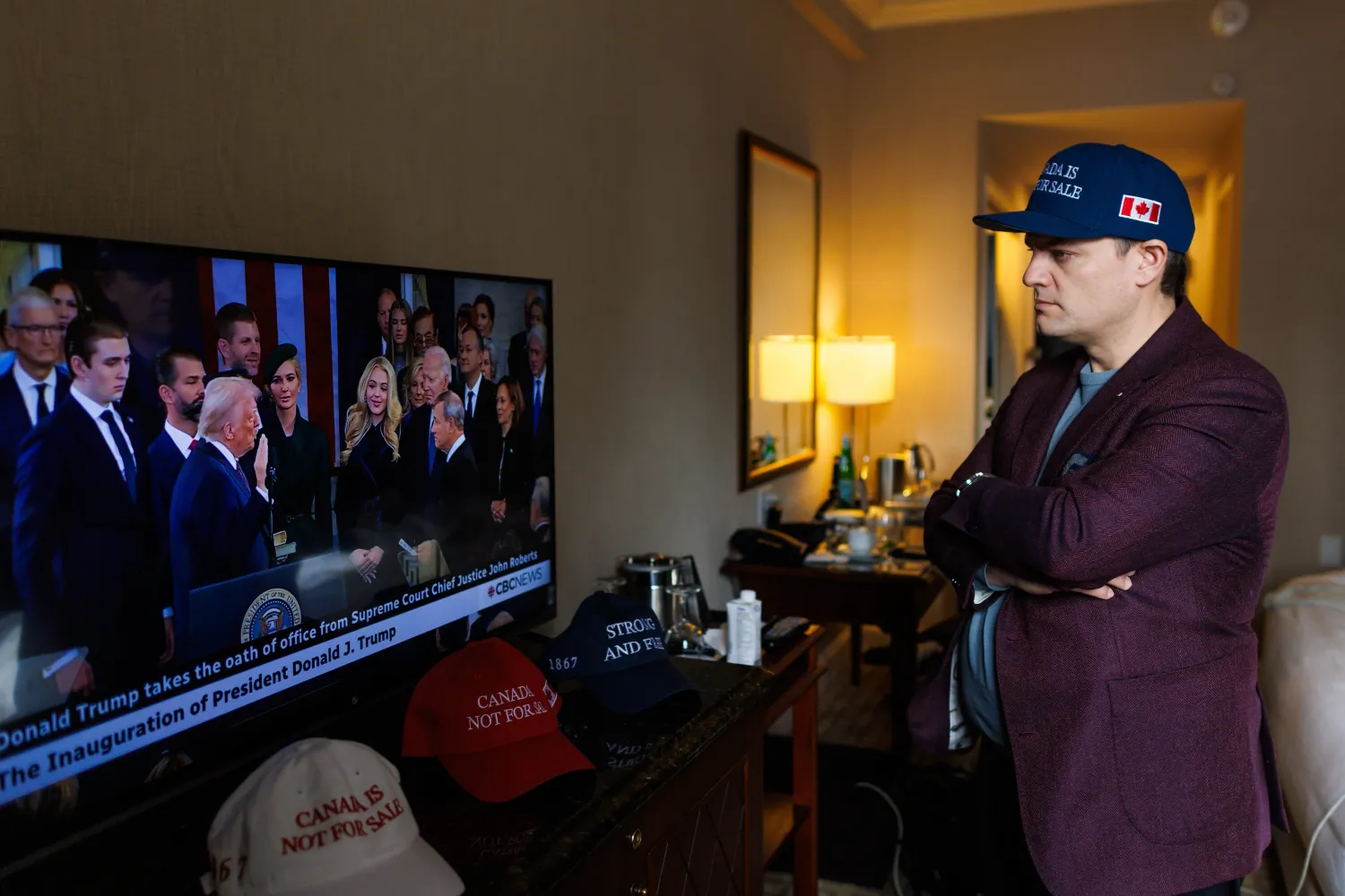 Man watches television coverage of U.S. President Donald Trump’s inauguration while wearing a dark blue hat with a Canadian flag on the side. 