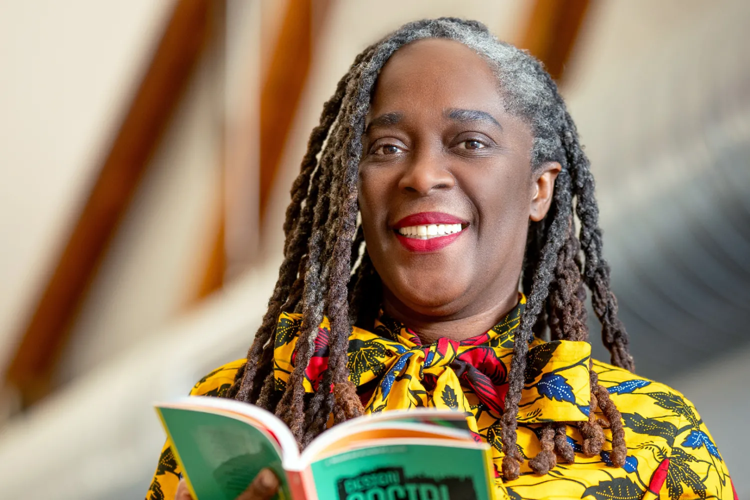 Photograph of Dr. Noel smiling into the camera while holding a book with a green cover in her hands. 