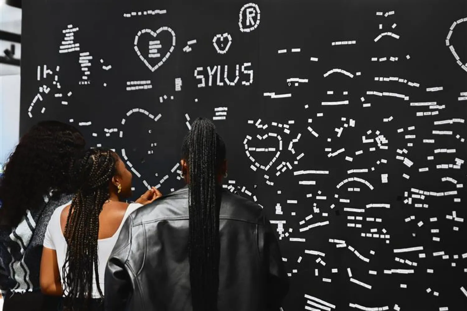Three women with long braids interacting with a poetry wall