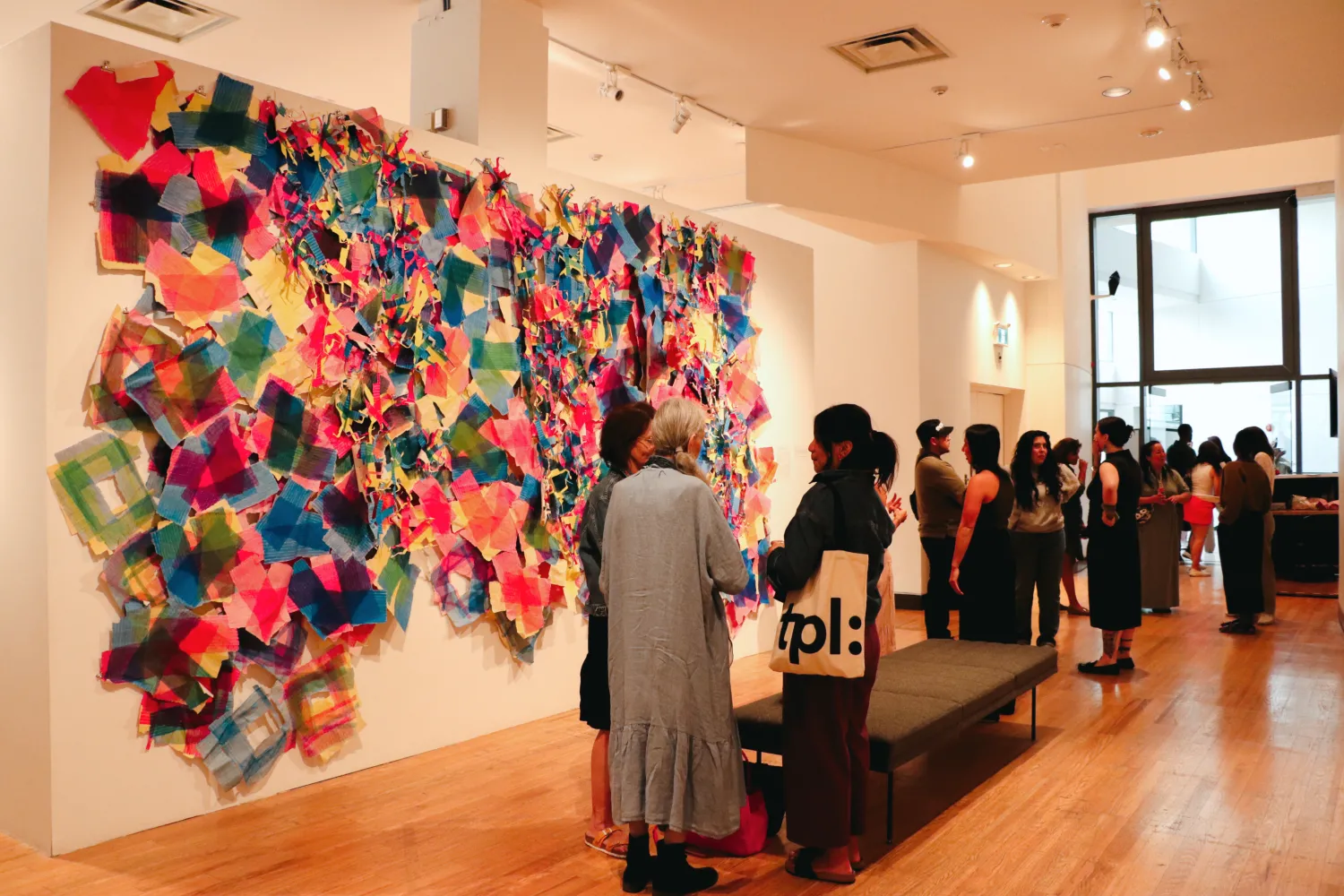 Group of people gathering at TO Live gallery with artwork by Laiken Breau displayed on the wall.