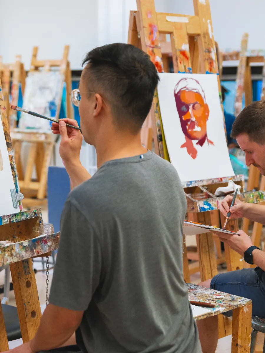 Two people sitting in front of easels painting with brown and orange.