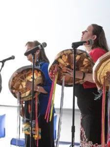 Four women playing musical instruments and singing into microphones.