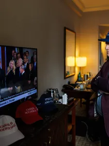 Man watches television coverage of U.S. President Donald Trump’s inauguration while wearing a dark blue hat with a Canadian flag on the side. 