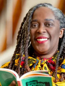 Photograph of Dr. Noel smiling into the camera while holding a book with a green cover in her hands. 