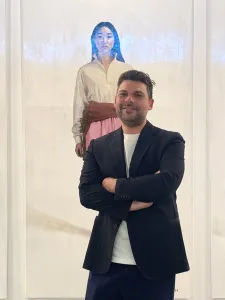 A man standing in front of three large paintings of stylish women.  