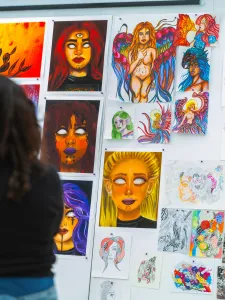 Person standing at a gallery wall covered in small paintings