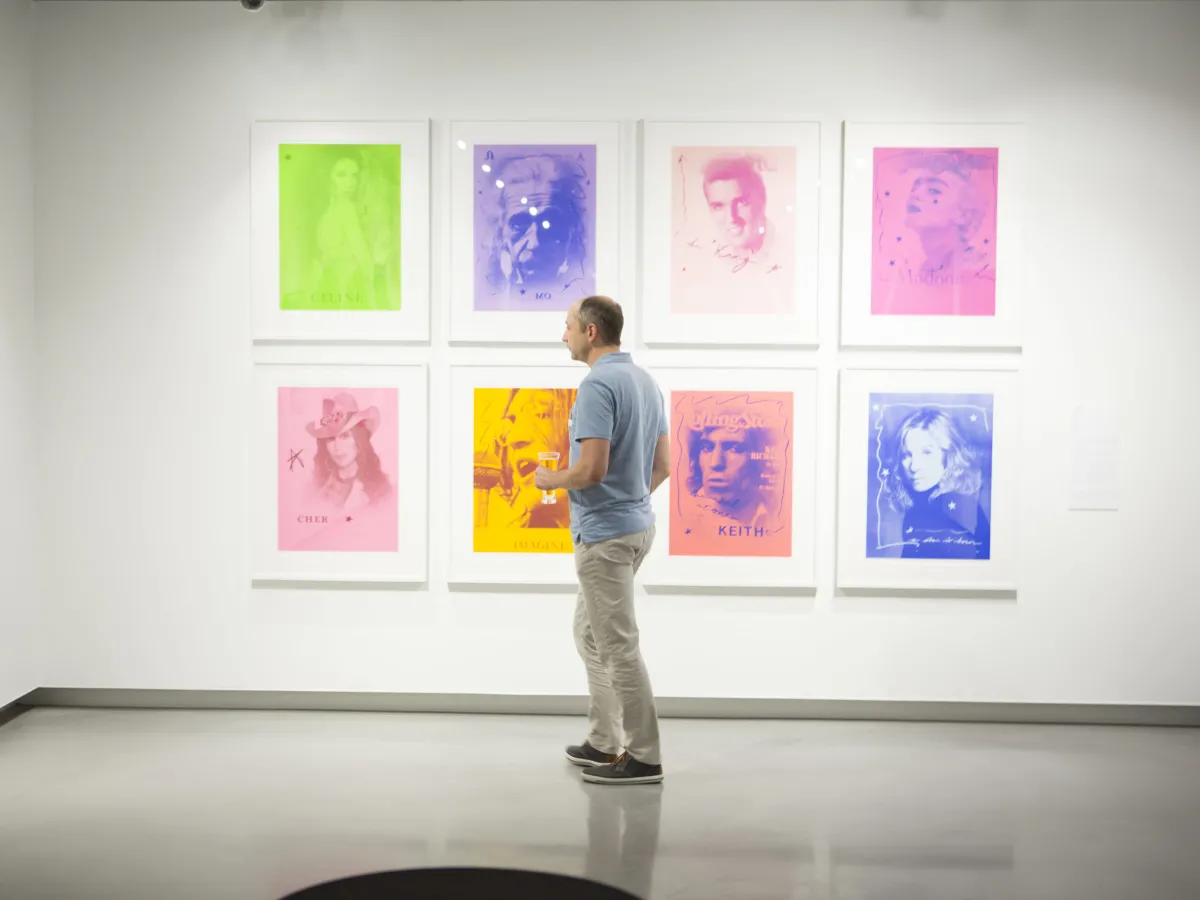 Person in a white room in front of eight pieces of art on the wall.