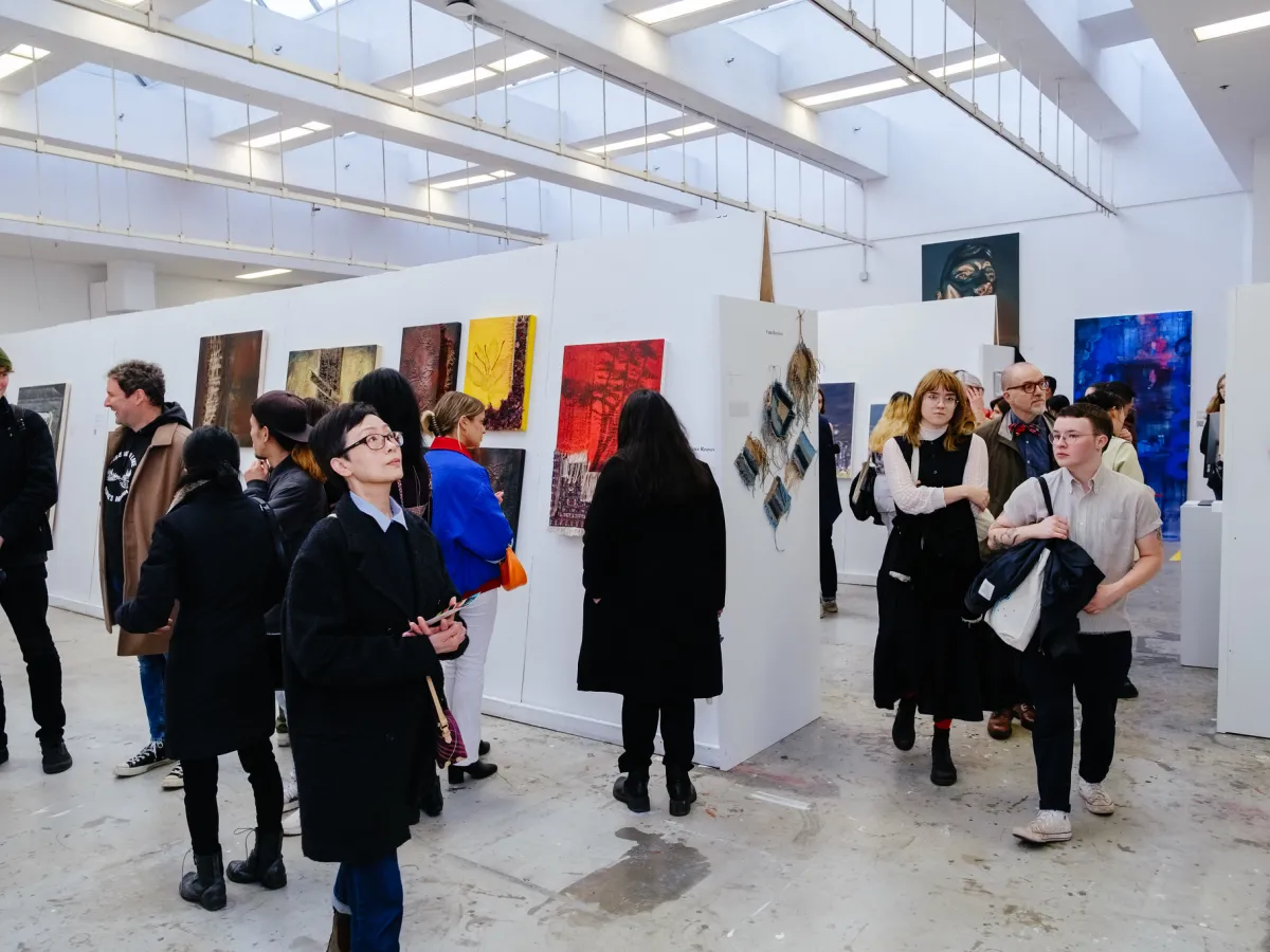 A group of people standing in an art gallery looking at art.