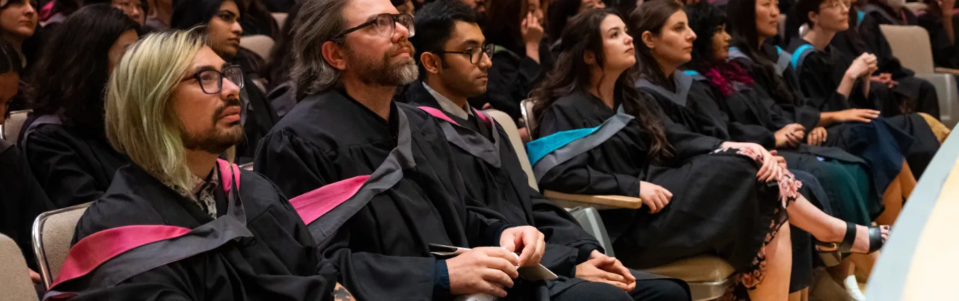 People in graduation robes, sitting in an auditorium looking forward.