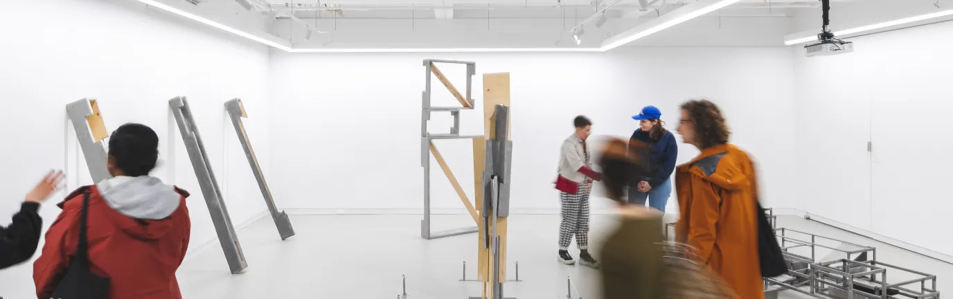 People in a white room with metal and wood frames.