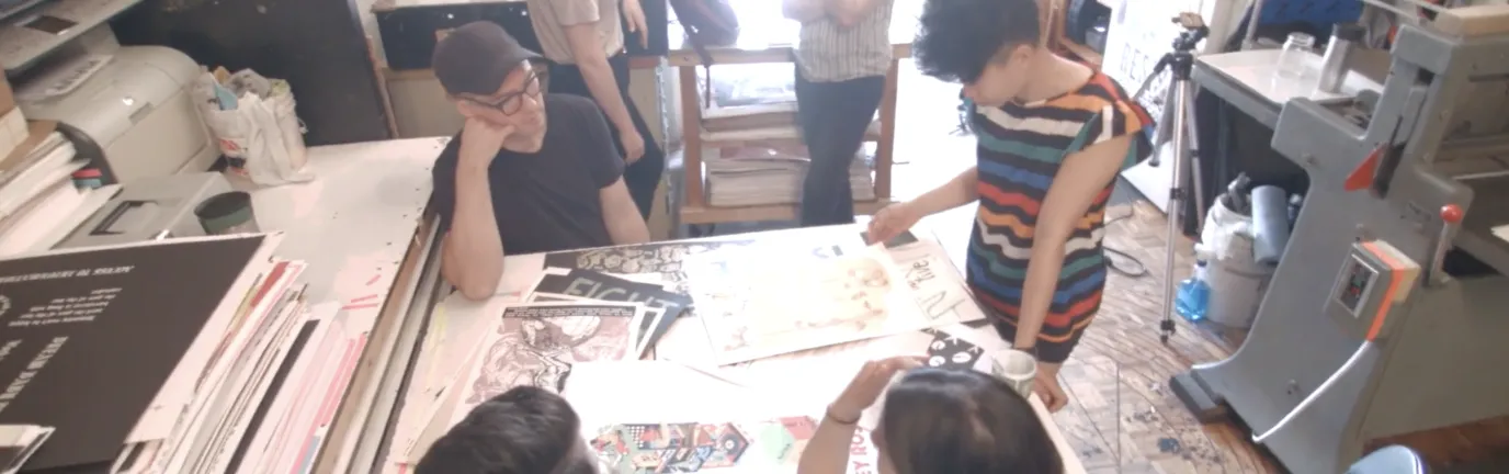 People standing and sitting around a table, looking at art.