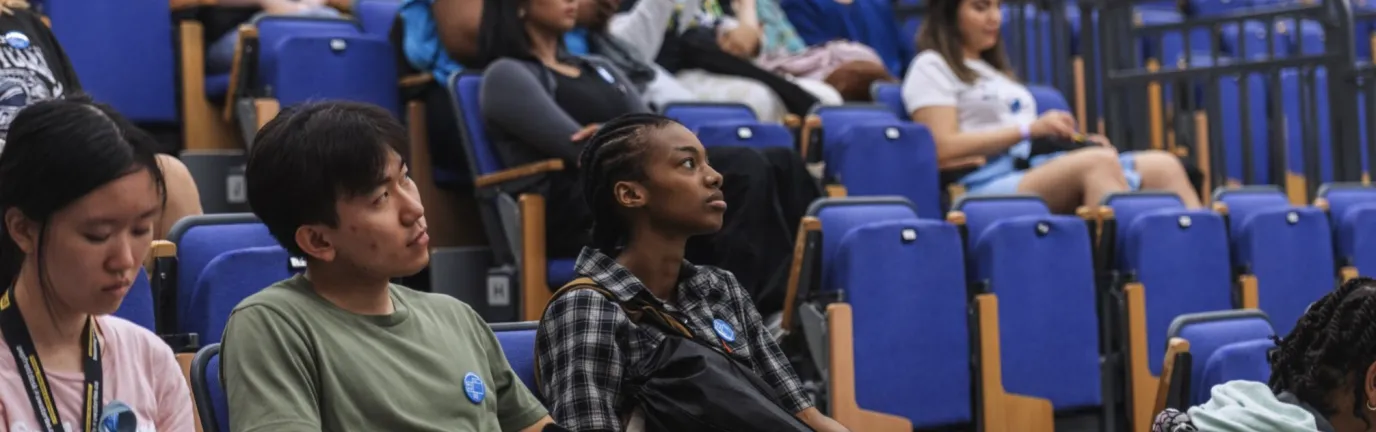 Rows of people sitting in an auditorium with blue chairs.