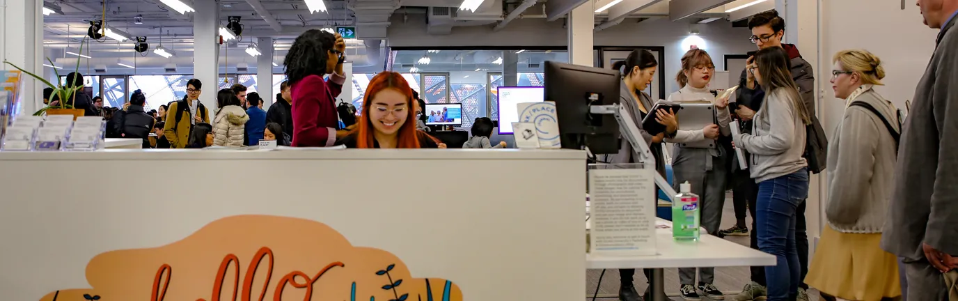 Group of people mingling behind a large white desk that says hello.