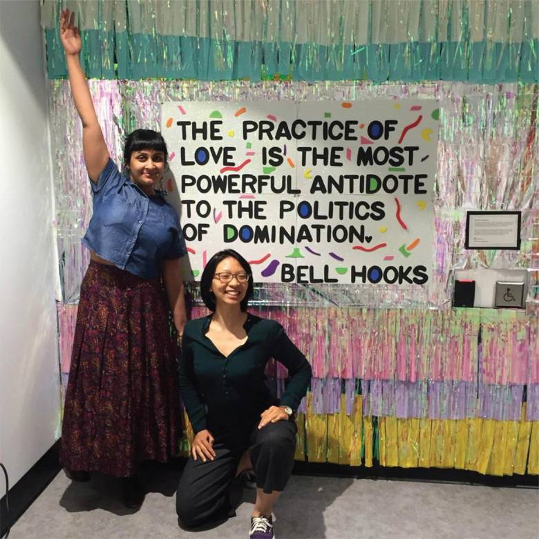 Image of Office of Diversity, Equity & Sustainability Initiatives staff Shamina Chherawala and Victoria Ho standing in front of a sign that says "The Practice of love is the most powerful antidote to the politics of domination", a Bell Hooks quote