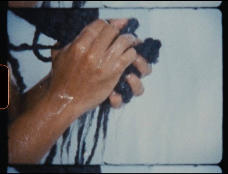 A frame of super film of a Black woman's hands holding her hair in a ball in the shower.