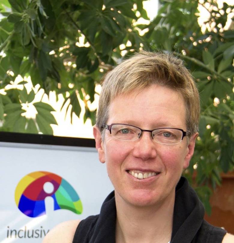 Photo of woman with short hair, wearing glasses and smiling with a tree in the background.