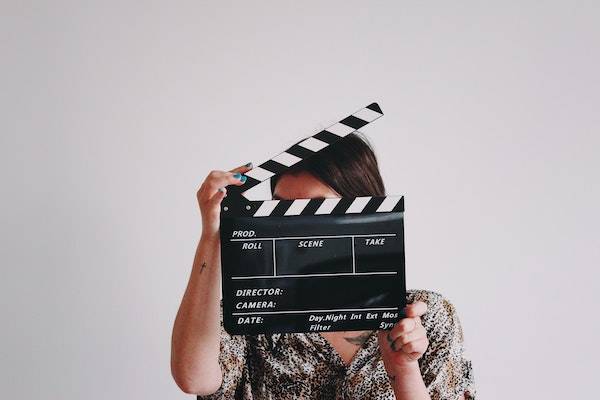 A photo of a person wearing a leopard print top holding a clapperboard in front of her face.