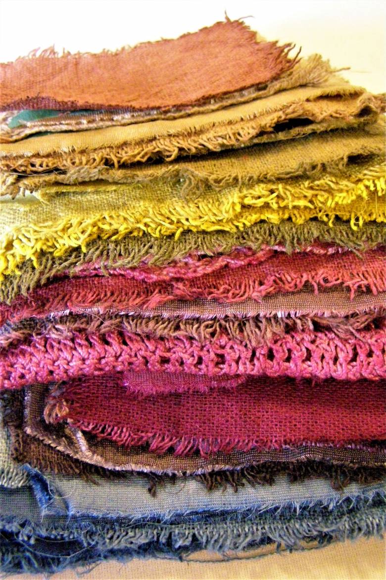    Nature Dye Fabric Stack - A collection of fabric samples from various tests. Colours from top to bottom are: madder, goldenrod, onion skin, marigold, cochineal, logwood and indigo.