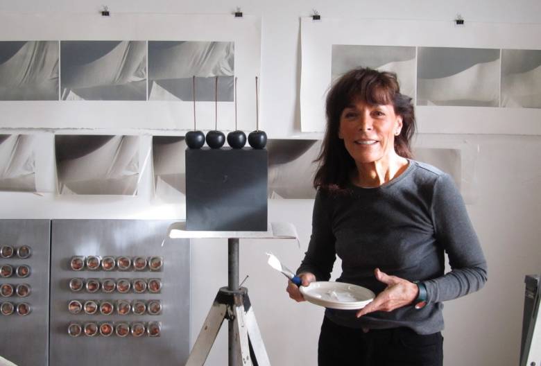 A photograph of Pixie Shaw in a studio holding a white ceramic palette in front of her work.