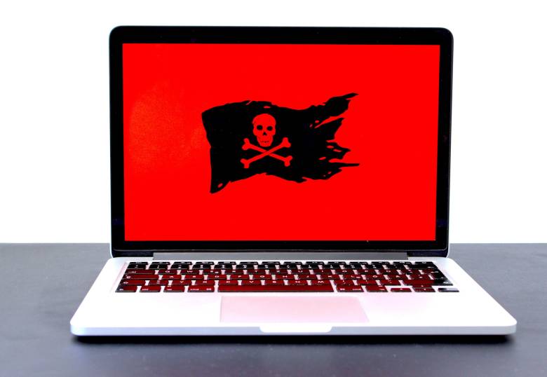 An image of a silver laptop on a dark table with a red and black pirate skull on the screen.