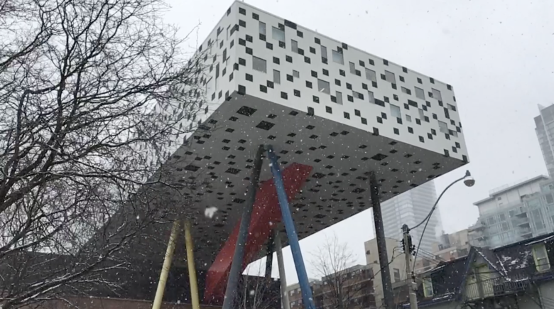 Photo of the Rosalie Sharp Centre for Design, a building that is a white square with block squares on stilts that are red, blue and yellow.  A bare tree is at the left with snowflakes coming down.
