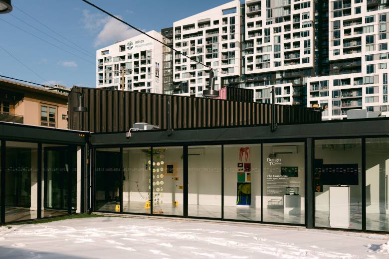 Image of black painted storefront with floor to ceiling windows against apartment buildings in background.