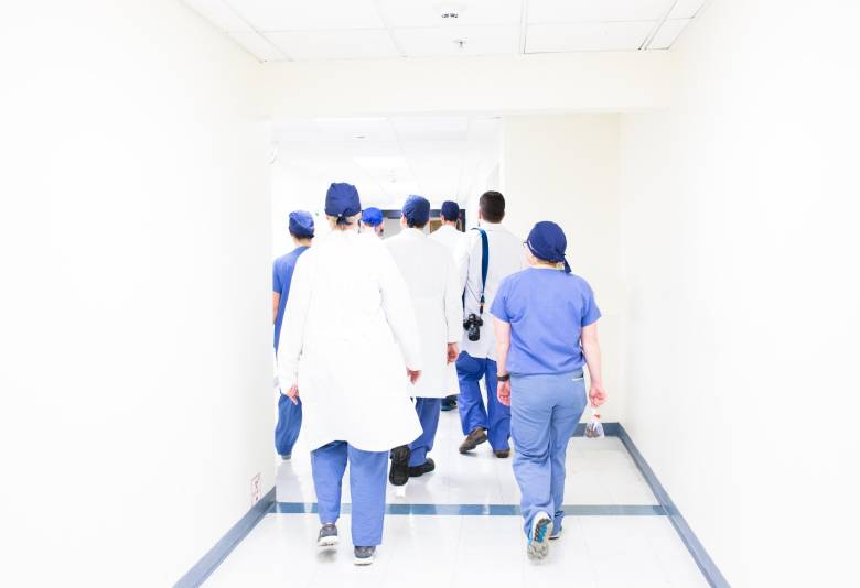 A group of doctors walking down a hospital hallway with their backs towards the camera.