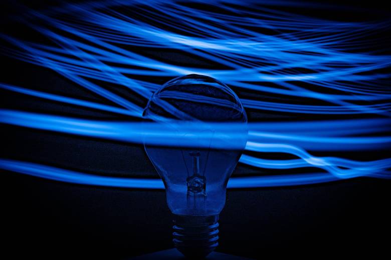 A photo of a light bulb with a black background. Blue strands of wire swirl around the light bulb.