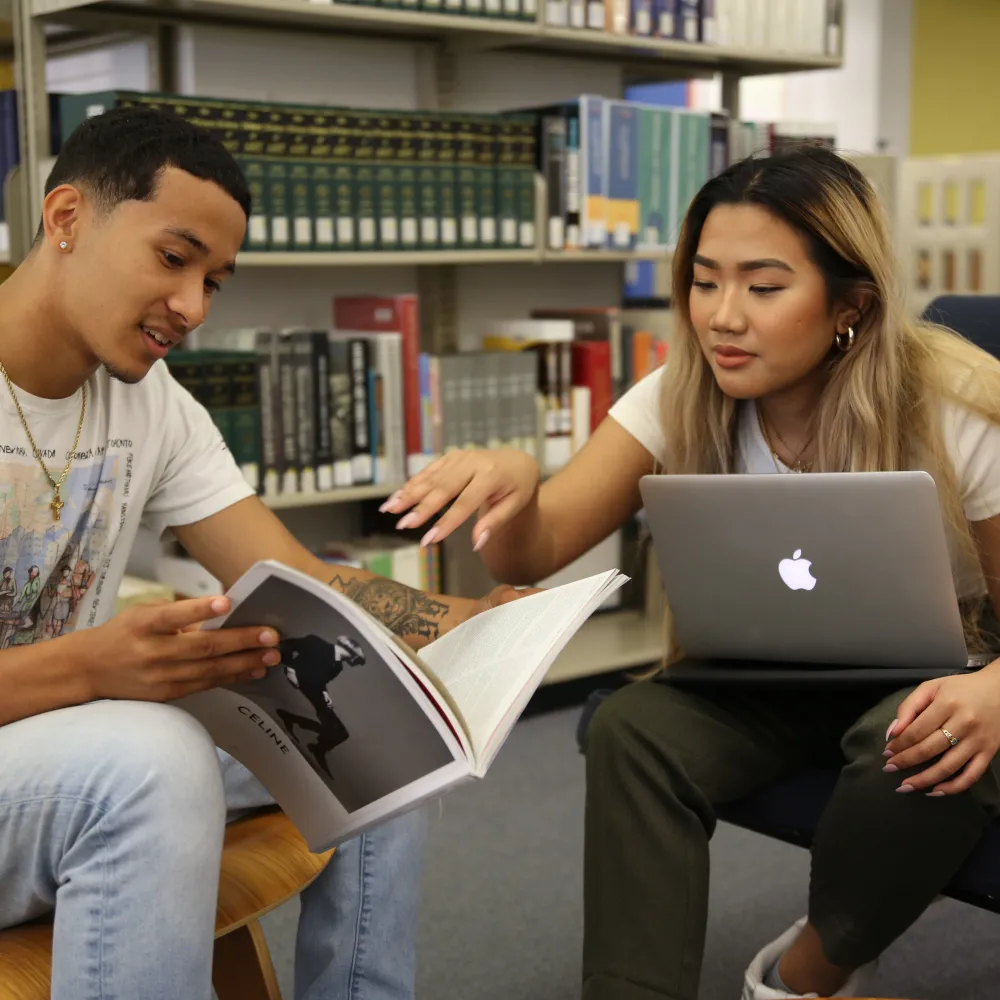 Two people sitting looking at an open book.