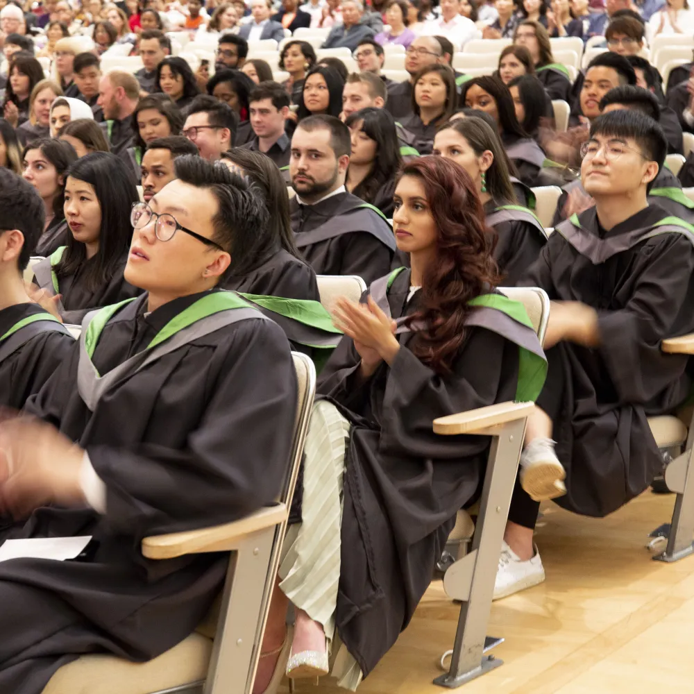 Students in graduation robes, sitting in an auditorium.