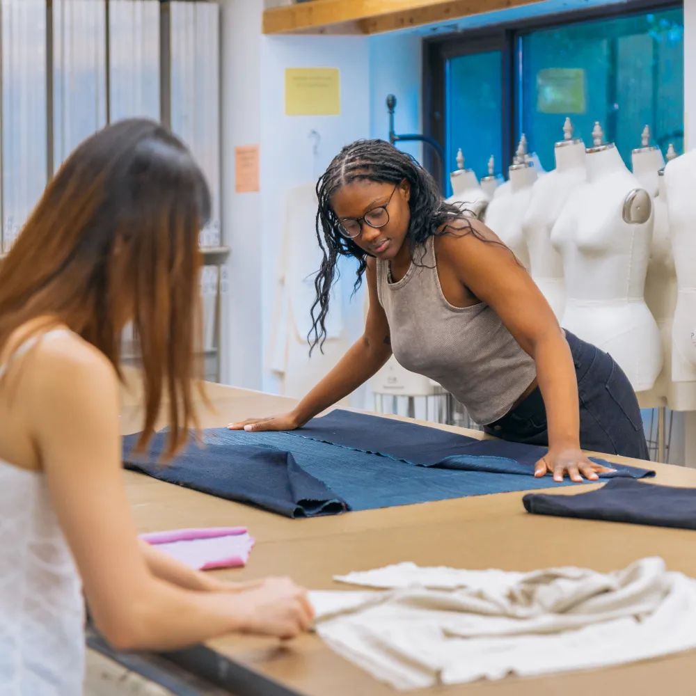 Two people working with fabric at a drafting table.