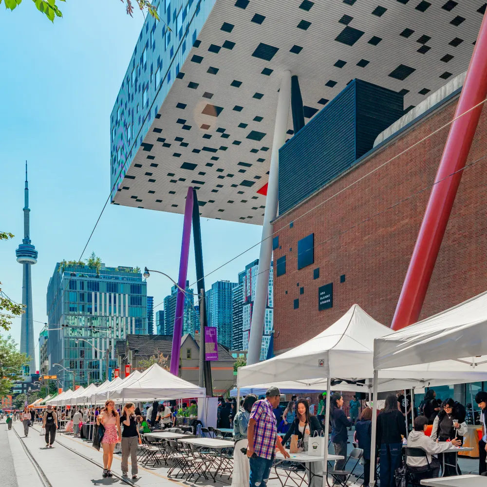 Shot of white and black checkered building with the CN Tower in the background.