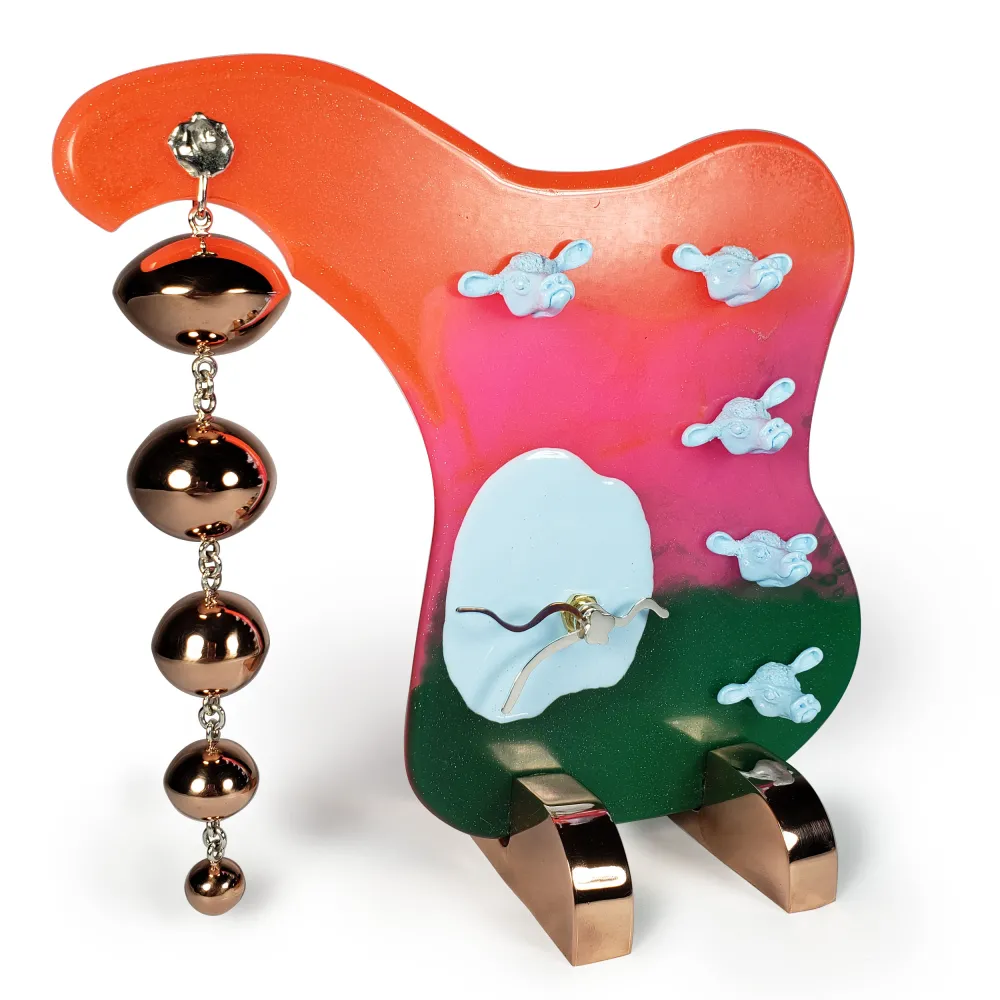 A colourful clock with faces of cows and dangling copper ellipsoids