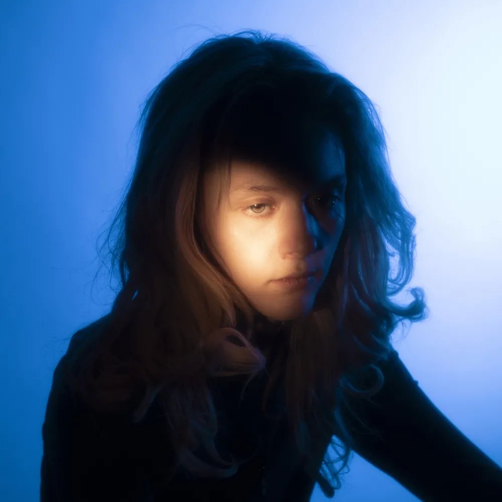 Photo of woman infront of blue background with a light shining on one side of her face