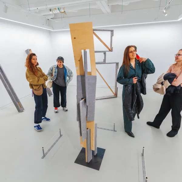 Group of people in a white art gallery with a wood sculpture