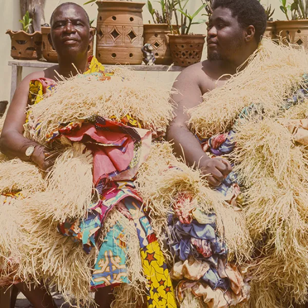 Photo of two people sitting on a bench wearing dried grass clothing